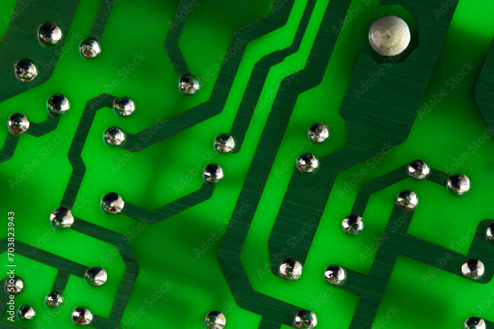 Conducting copper traces with silver drops of solder on a green backlit