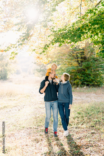 Mom hugs dad with a little boy on his shoulders, walking in the autumn park © Nadtochiy