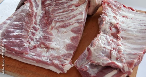 Pork preparation for oven roasting, arranging piece of pork belly, cutting off ribs using knife, close-up photo