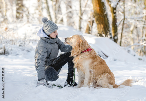 Teenage Girl And Golden Retriever Sit Together In Snow-Covered Forest During Winter © tan4ikk