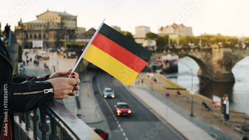 Young Woman Holds German Flag In Hand, With Blurred City Background In Autumn