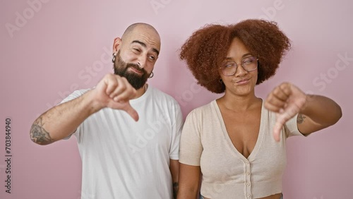 Cool couple, the epitome of relaxed lifestyle, standing together in negative expression over isolated pink. beautiful man and woman throwing down a serious, bad ass thumb-down gesture