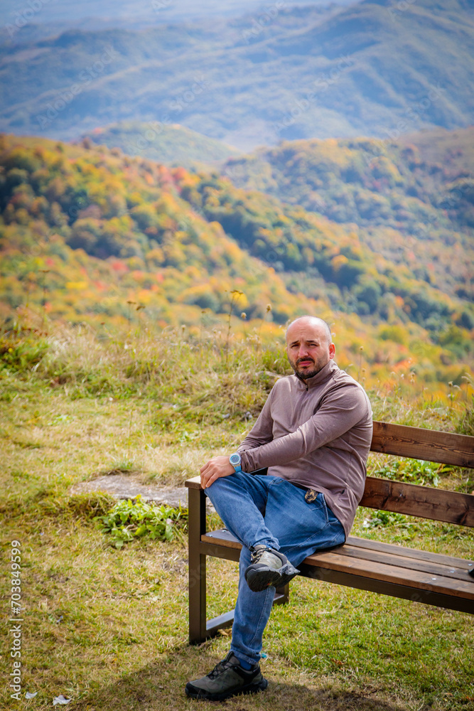 Serene Man Sitting on Wooden Bench Enjoying Scenic View of Majestic Mountain Landscape Serene Man Sitting on Wooden Bench Enjoying Scenic View of Majestic Mountain Landscape