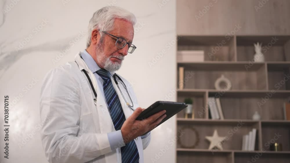 Mature senior male doctor in medical uniform using digital tablet in clinic. Therapist professional healthcare expert searching information online in hospital room. Medicine healthcare medical checkup Mature senior male doctor in medical uniform using digital tablet in clinic. Therapist professional healthcare expert searching information online in hospital room. Medicine healthcare medical checkup
