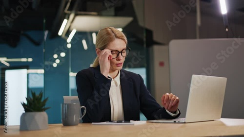 Overtired businesswoman in a blue suit and glasses in the office. Woman feels tired from work, takes off glasses rubs temples to ease headache. Female person suffers from headaches and lack of sleep. photo