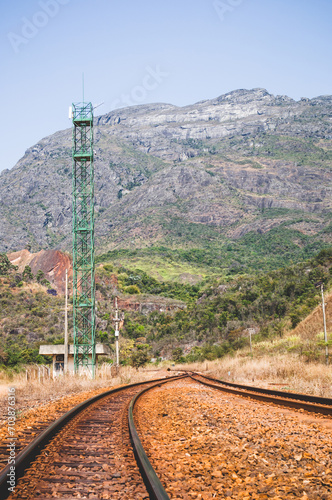 As montanhas no interior de Minas Gerais com o detalhe principal da linha ferra com os dormentes e britas e uma torre de comunicação com uma edificação photo