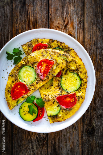 Omelette - scrambled eggs with mozzarella cheese, zucchini and tomatoes on wooden table
