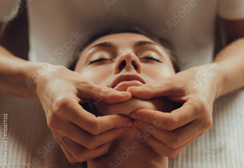 Hands of female chiropractor massaging face of young woman lying on massage table. Visceral massage. Concept of physical therapy treatment, neck pressure point photo