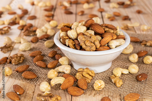 Assorted nuts - almonds, cashews, hazelnuts or filberts, walnuts, in white bowl on wooden background.