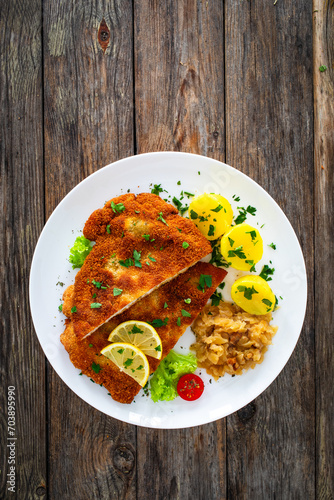 Crispy breaded fried cutlet with boiled potatoes and cooked cabbage on wooden table
