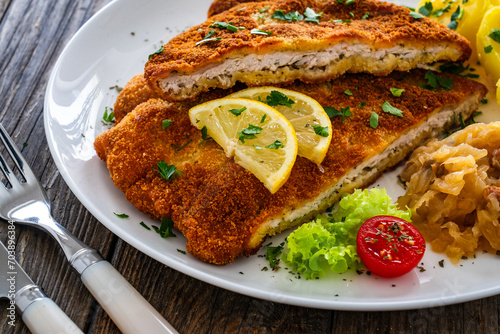 Crispy breaded fried cutlet with boiled potatoes and cooked cabbage on wooden table
