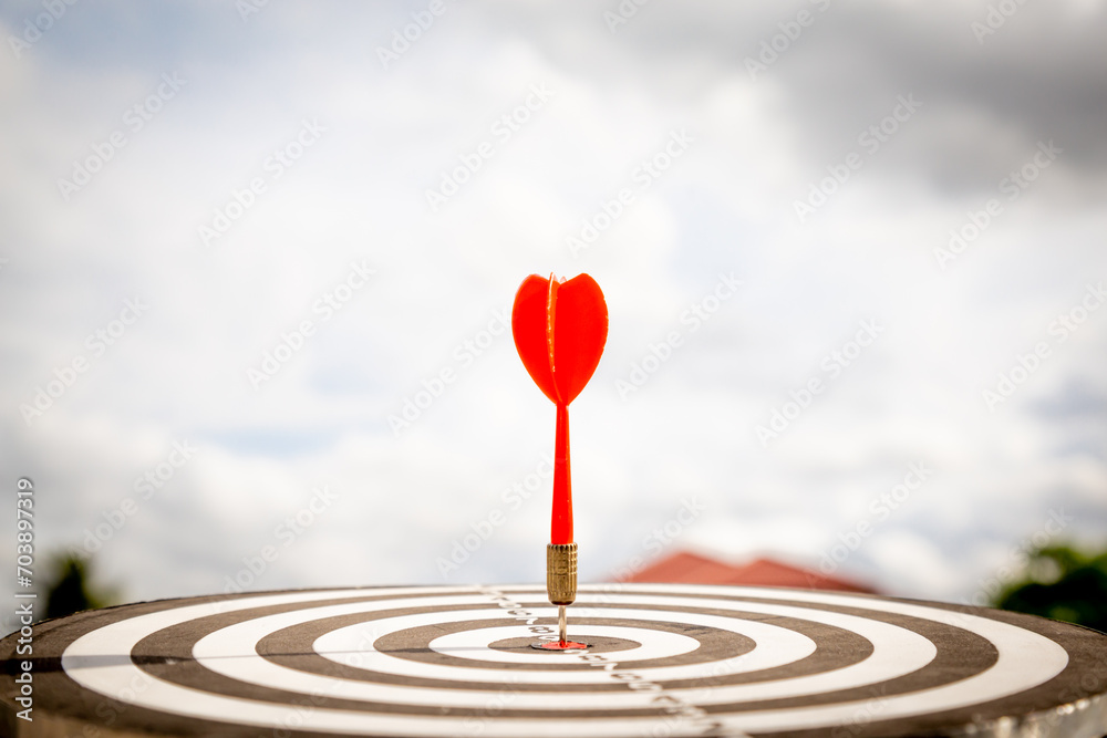 Close up shot red darts arrows in the target of dartboard center on dark blue sky background. Business target or goal success and winner concept. Close up shot red darts arrows in the target of dartboard center on dark blue sky background. Business target or goal success and winner concept.
