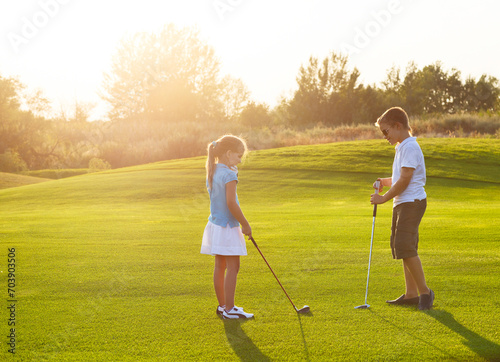 Kids at a golf field holding golf clubs. Sunset