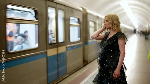 beautiful blonde woman in elegant chiffon dress standing on metro station and looking to train photo