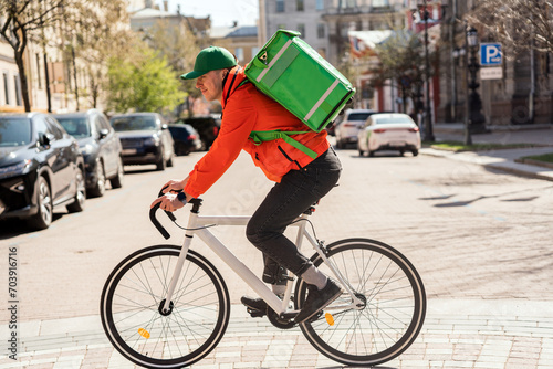 Delivery cyclist in vibrant gear navigates the city streets with a green insulated backpack. © muse studio