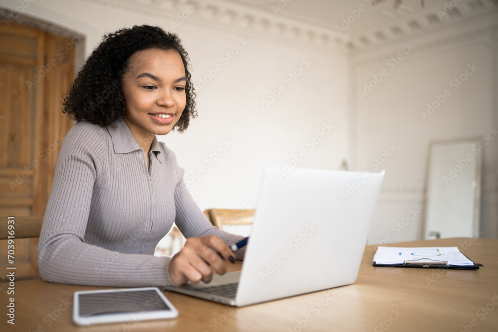 Focused young woman working on a laptop with a tablet beside her in a bright, elegant room. Focused young woman working on a laptop with a tablet beside her in a bright, elegant room.