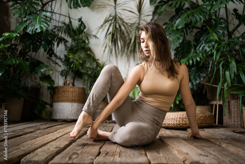 Relaxed woman in athleisure wear stretches in a home filled with lush green plants. photo