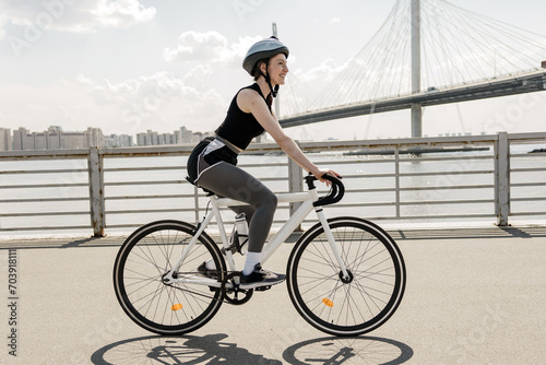 Urban cyclist enjoys a sunny ride along the river, helmet on for safety.