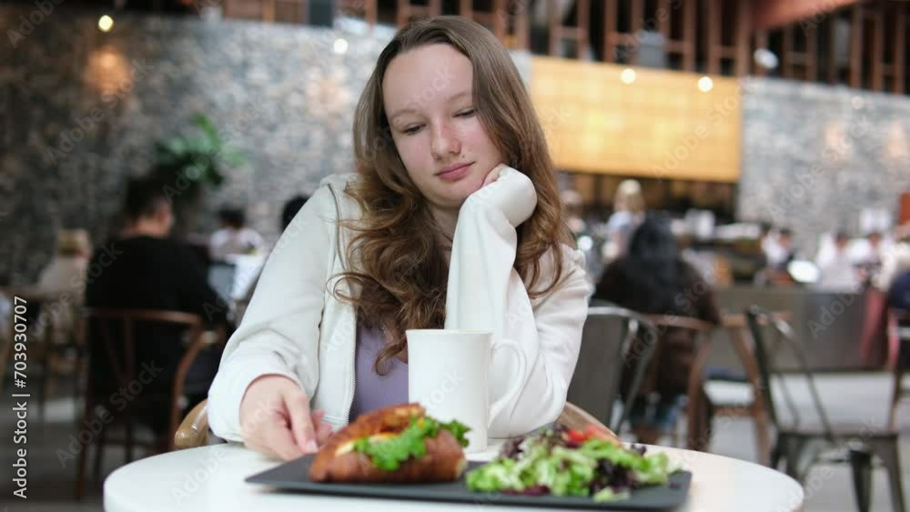 A young girl woman has breakfast in cafe restaurant with a croissant and salad on black plate, pleasant emotions, smile,joy of spending time traveling, being alone with white cup. diet lots of greens A young girl woman has breakfast in cafe restaurant with a croissant and salad on black plate, pleasant emotions, smile,joy of spending time traveling, being alone with white cup. diet lots of greens