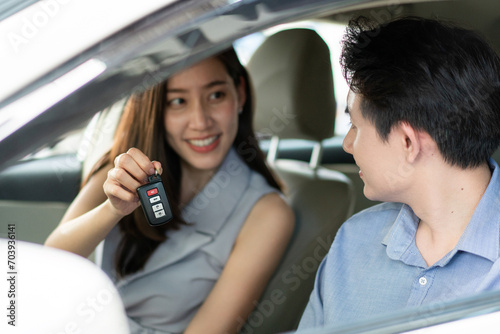 Happy Asian young woman showing remote car to her friend or boyfriend sitting in vehicle at automotive rental, customer satisfied feedback, test driving, dealership or purchasing concept, focus on key © winnievinzence
