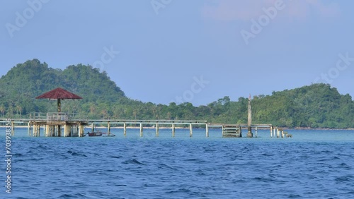 Floating wooden house lodge on stilts with musholla on calm blue-green water with green tropical island in the background photo