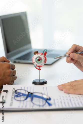 Close-up of an Asian male doctor showing an eyeball model and explaining eye diseases to a male patient in hospital. health care concept