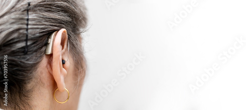 Photo of the back of an ear of an unrecognizable older woman with a behind-the-ear hearing aid on a white background.Amplify sound.Advertising hearing aids.Copyspace for advertising. photo