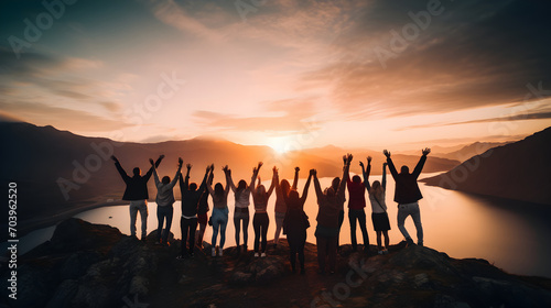 Group of people have fun in success, happy pose of people with raised arms on mountain top against sunset lakes and mountains