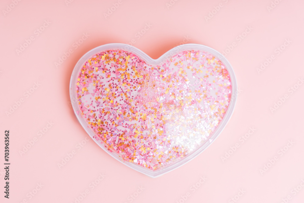 Plastic heart with sparkles inside on a pink background.