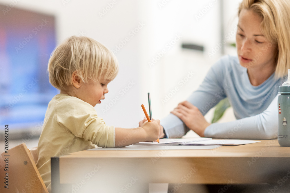 Caring young Caucasian mother and small son drawing painting in notebook at home together. Loving mom or nanny having fun learning and playing with her little 1,5 year old infant baby boy child Caring young Caucasian mother and small son drawing painting in notebook at home together. Loving mom or nanny having fun learning and playing with her little 1,5 year old infant baby boy child