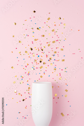 White champagne glass with confetti on pink background. Minimal party concept.