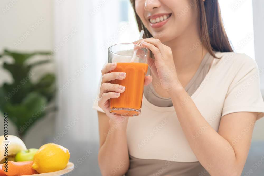 Orange detox juice concept, smile asian young woman hand holding a glass of vegetable juice, carrot smoothie for diet at home, drinking healthy meal food for weight loss. Lifestyle, vegan nutrition. Orange detox juice concept, smile asian young woman hand holding a glass of vegetable juice, carrot smoothie for diet at home, drinking healthy meal food for weight loss. Lifestyle, vegan nutrition.