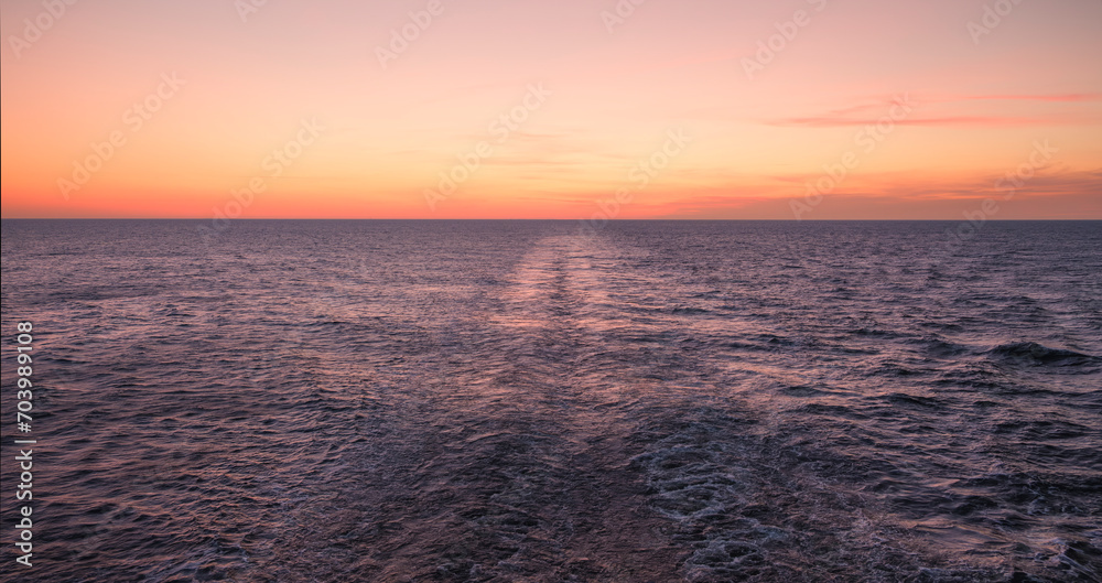 Beautiful red sunset over the blue sea horizon behind the stern of a sailing ferry ship