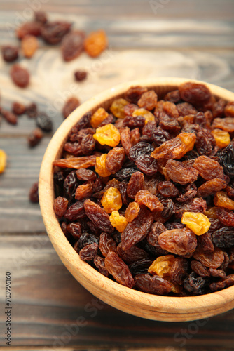 Dry raisins in wooden bowl on brown wooden background. Vertical photo