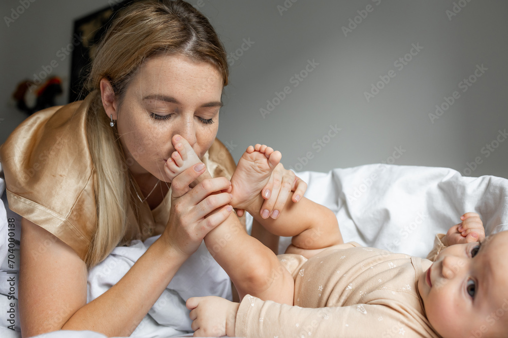 Closeup side view of a mother kissing her baby leg on bed at home Closeup side view of a mother kissing her baby leg on bed at home
