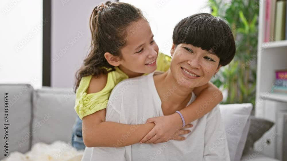 Confident mother and daughter sharing a joyful hug, smiling heartily while sitting on the living room sofa at home – a beautiful expression of family love and happiness Confident mother and daughter sharing a joyful hug, smiling heartily while sitting on the living room sofa at home – a beautiful expression of family love and happiness