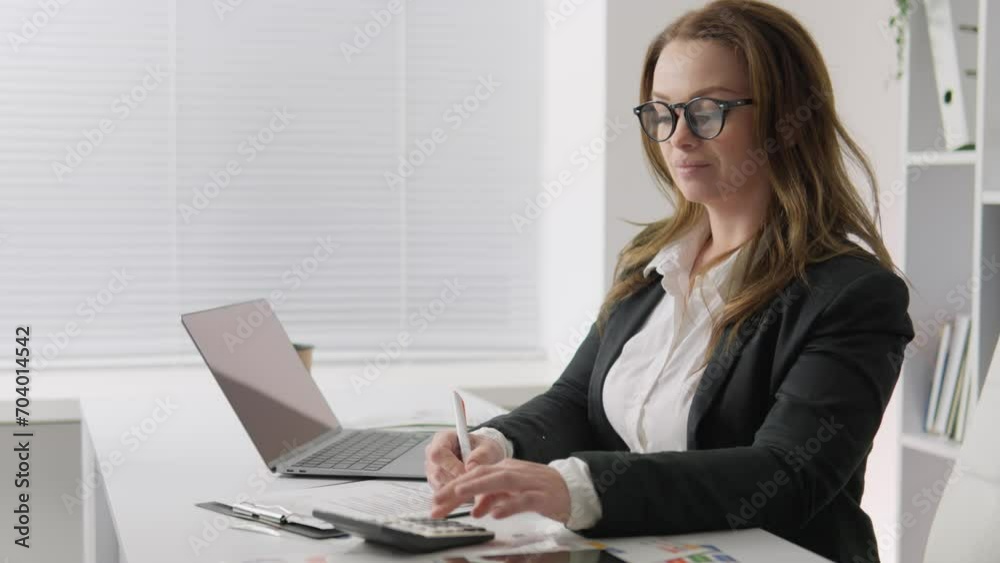 An economist conducts a financial audit and evaluates performance using a calculator and a computer in her office. The woman provides advice on tax issues and keeps records of financial transactions An economist conducts a financial audit and evaluates performance using a calculator and a computer in her office. The woman provides advice on tax issues and keeps records of financial transactions