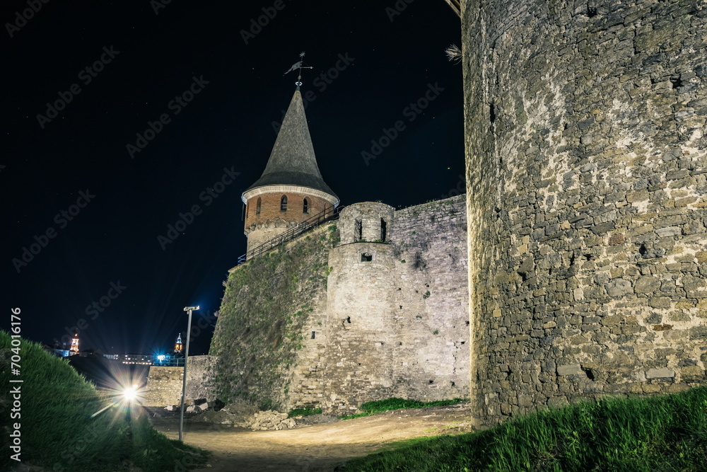 View of the towers and walls of the Kamianets-Podilskyi Castle in the night. Stone bastion of an ancient castle. Beautiful stone castle on the hill at night. Ukraine