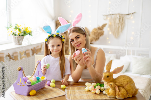 easter, a mother with a little daughter with hare ears on her head are preparing for the holiday by coloring eggs and playing with them, lifestyle, preparing a happy family with a child for Easter