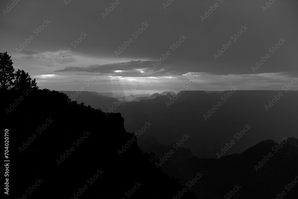 Evening sunbeams streaming through the clouds creates a dramatic black and white photo of silhouetted ridgelines in Grand Canyon National Park after a stormy August day in Arizona, USA.