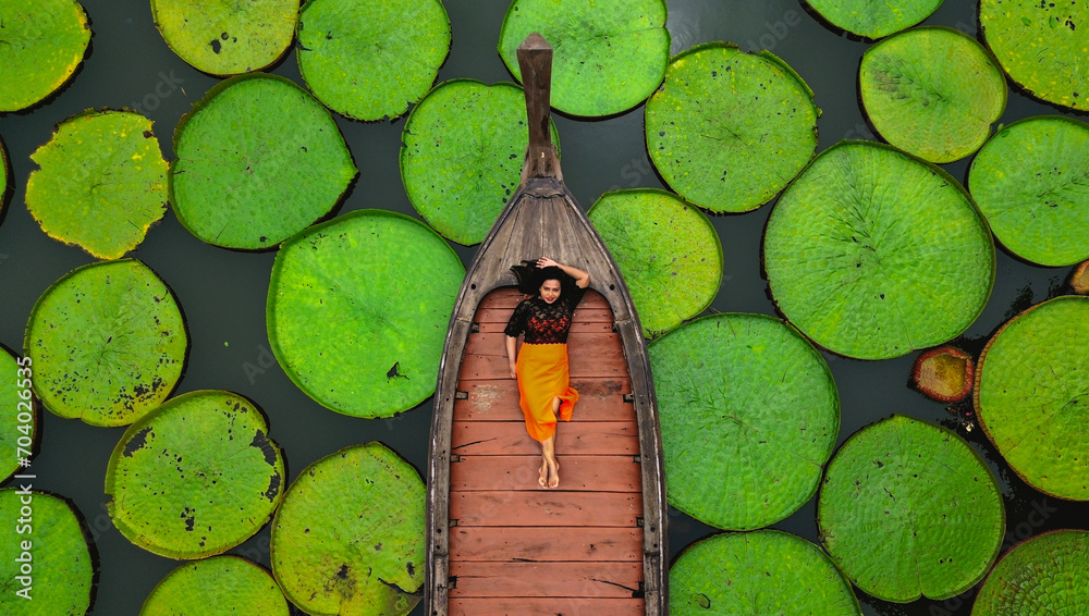 Fototapeta premium Aerial view of an Asian woman relaxing on a boat outdoor on Lotus pond at Phuket Thailand