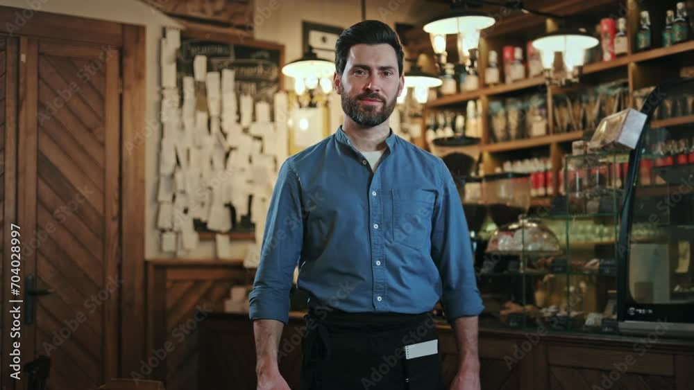 Satisfied caucasian waiter wearing dark blue shirt doing positive gesture with hand in restaurant interior. Cheerful bearded male expression happiness and demonstrating agreement with thumb up. Satisfied caucasian waiter wearing dark blue shirt doing positive gesture with hand in restaurant interior. Cheerful bearded male expression happiness and demonstrating agreement with thumb up.