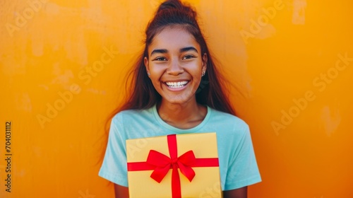 Happy woman holding gift box rejoicing in birthday or Christmas surprise received. Smiling girl in casual T-shirt holds out box with bow to congratulate loved one on holiday photo