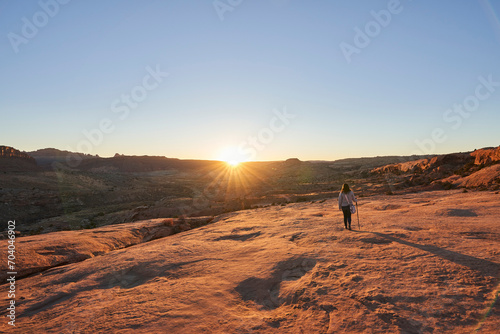 The sun sets over the distant mountains, as a female hiker takes in the golden view.