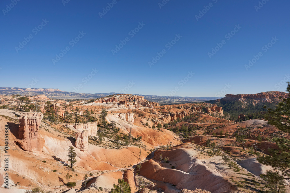 These sand dunes are found in Bryce Canyon National Park. They are very colorful, with orange, white, and red coloring. A few rock hoodos sprout of the landscape, that is formed by erosion.