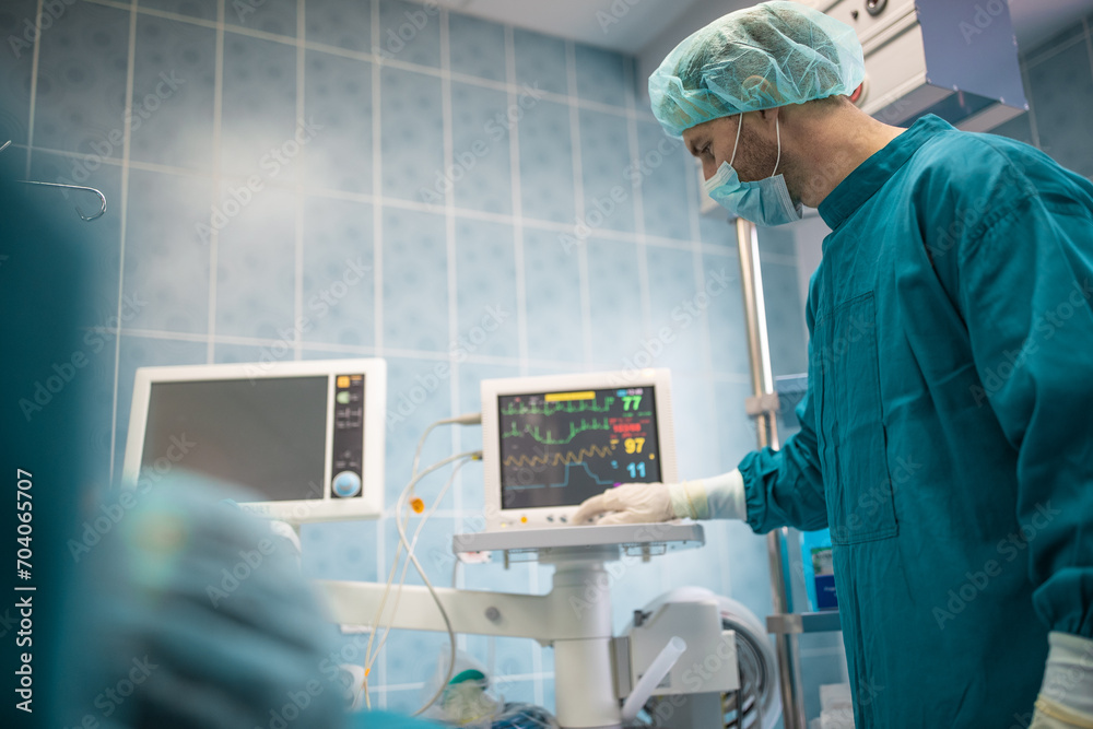 Male surgeon keeping track of vital functions of the body during cardiac surgery. Surgeon looking at medical monitor during surgery. Doctor checking monitor for patient health status. Male surgeon keeping track of vital functions of the body during cardiac surgery. Surgeon looking at medical monitor during surgery. Doctor checking monitor for patient health status.