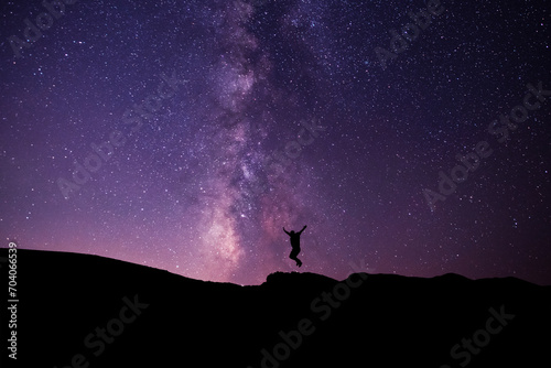 Silhouette of a hiker jumping on the hill, on the milky way galaxy background.