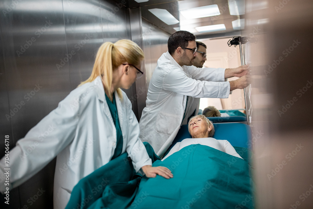 Two medical professionals male and female with sleeping patient on a gurney in elevator. Two medical professionals male and female with sleeping patient on a gurney in elevator.