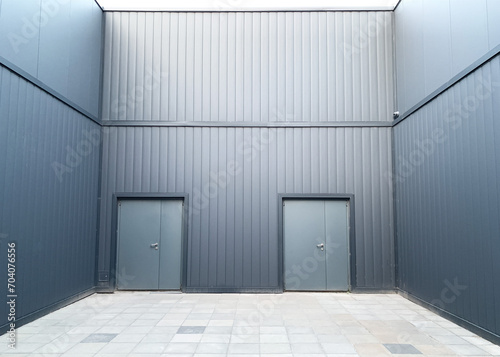 Two gray metal entry doors in a wall covered with facade slatted panels.