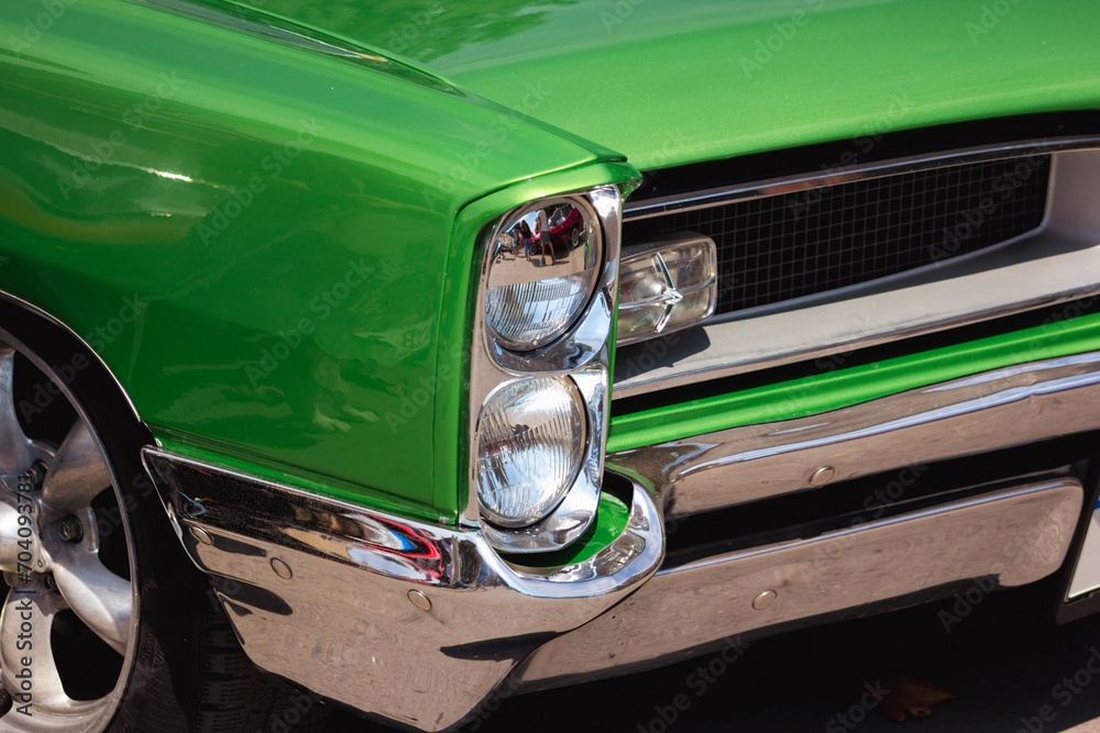 Green retro car with close-up on headlight. Front view muscle car oldtimer with chromed bumper